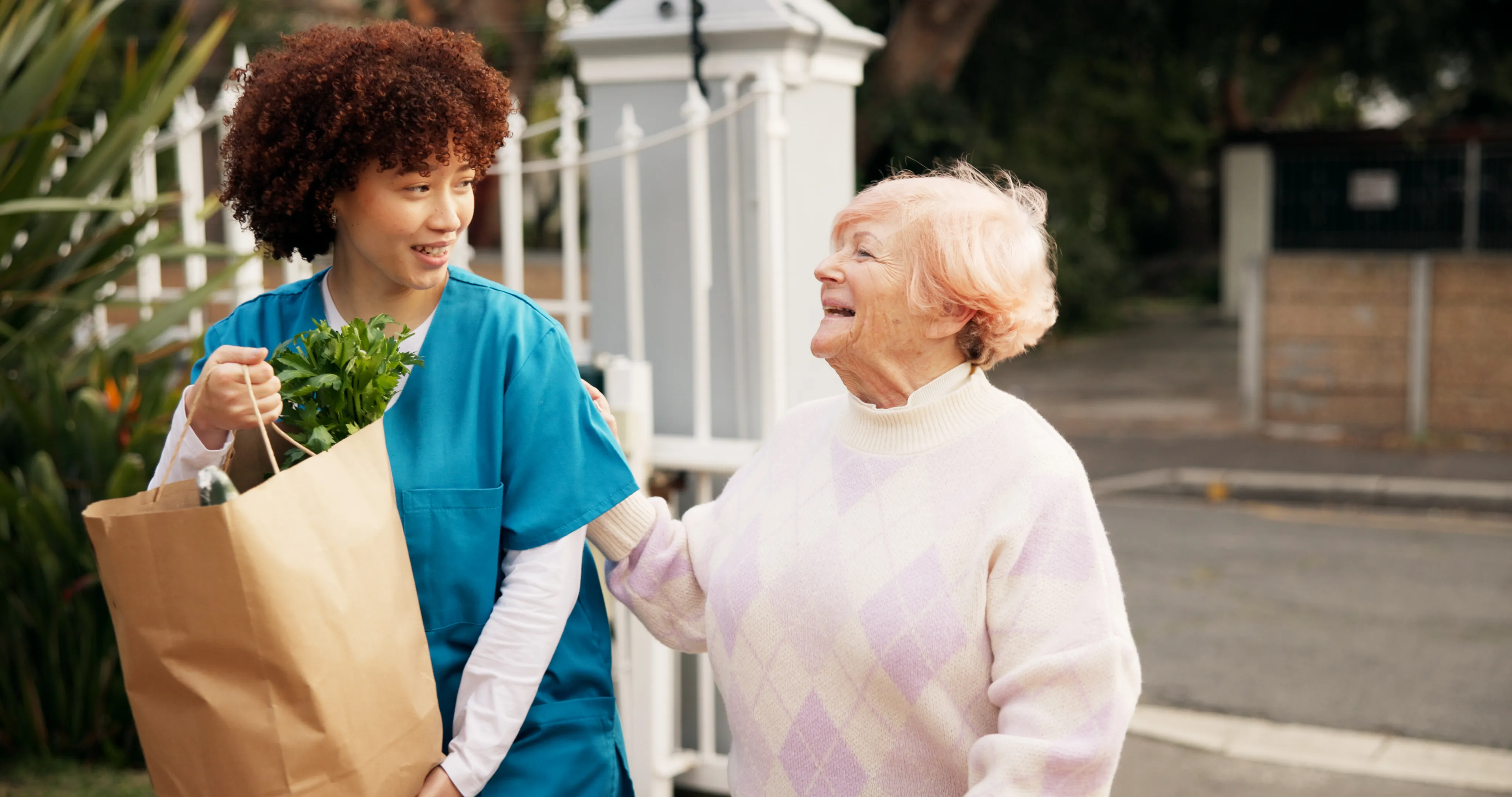 Morning Star caregiver carries groceries while sharing a warm moment with a smiling senior outdoors.